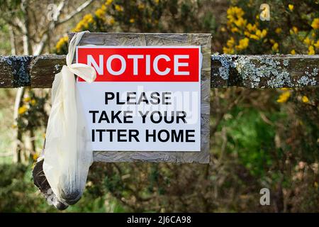 DISCARDED BAG FULL OF DOG FAECES LEFT BY IRRESPONSIBLE OWNER ON A COUNTRY FOOTPATH WITH A WARNING SIGN Stock Photo