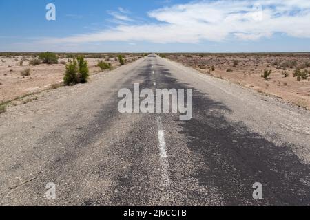 Long straight deserted road through desert in Uzbekistan showing road, scrub and vanishing point with clouds in sky Stock Photo