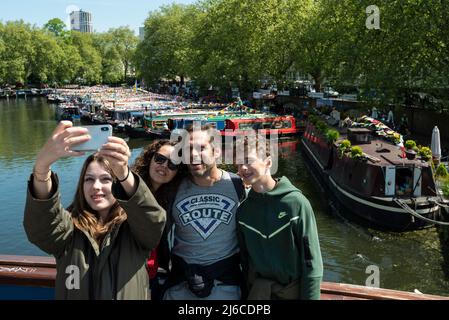 London, UK.  30 April 2022.  A family takes a selfie against a background of narrowboats decked out with colourful bunting and other festival-style decorations during the Inland Waterways Association (IWA) Canalway Cavalcade in Little Venice to celebrate the best of life on the waterways in London and its community.  The event takes place over the early May Bank Holiday weekend and after being cancelled due to the pandemic, this year’s theme is “Welcome Back”.  Credit: Stephen Chung / Alamy Live News Stock Photo