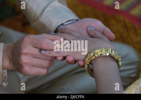 Thai wedding: a groom is putting on a golden ring to a bride's finger Stock Photo