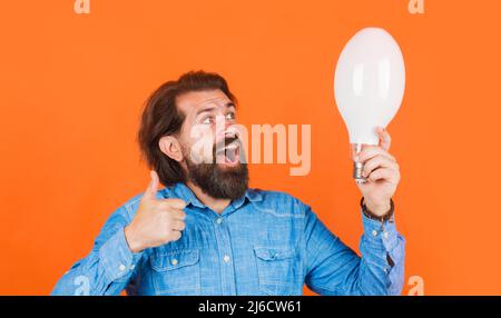Good idea. Happy man with light bulb showing thumb up. Bearded male with big lamp in hand. Stock Photo