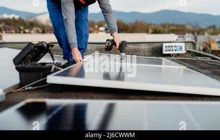 Solar panel technician with drill installing solar panels on roof on family house a sunny day Stock Photo