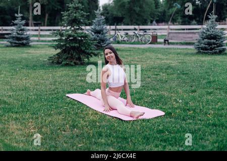 Happy young woman trains in nature. Shot of attractive brunette doing yoga in splits pose in park on hot summer morning Stock Photo