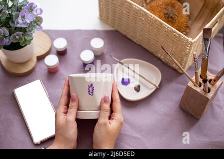 Womens hands hold a white flower ceramic pot on the table with craft tools Stock Photo