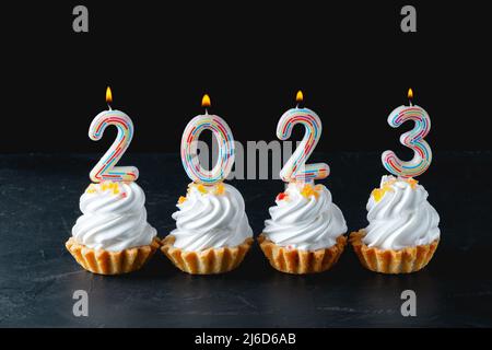 Festive cupcakes and candles in form of numbers 2023 on black background. Stock Photo