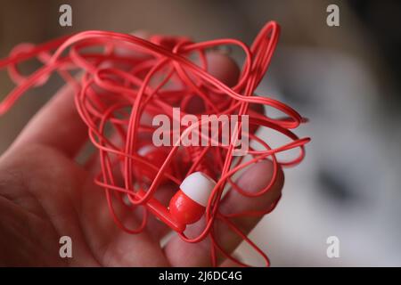 Tangled red headphones in hand closeup. Person trying to unravel broken headphones Stock Photo