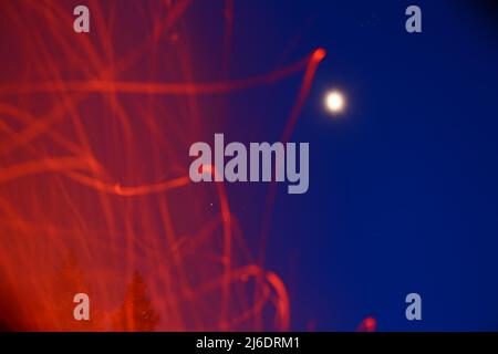 Trails of defocused sparks in front of sky with bright moon and stars. Stock Photo