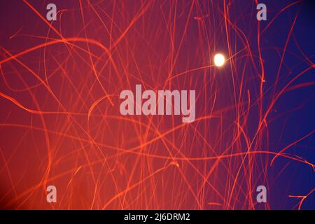 Trails of defocused sparks in front of sky with bright moon and stars. Stock Photo