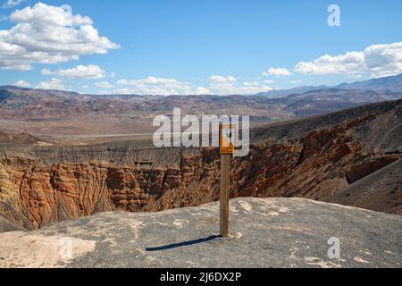 Desert hiking, Ubehebe Crater view point and warning sign 'Use caution near the edge' in Death Valley National Park, California Stock Photo