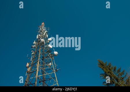 Tv or radio antenna, communications tower on the top of the hill on a small clearing and blue skies. Antenna above Lasko at Malic on a sunny day. Stock Photo