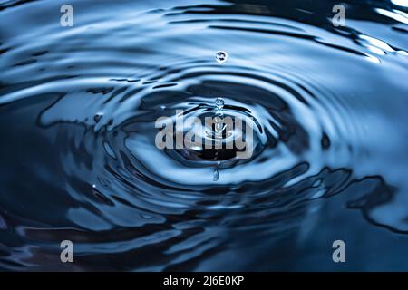 Drops and ripples, splash. Close-up of blue water rings, circular reflections, waves on the liquid surface. Stock Photo