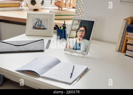 Focus on digital tablet with tutors portrait on table with open workbook and school supplies Stock Photo