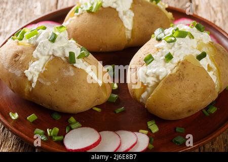 Boiled jacket potatoes stuffed with cottage cheese, sour cream and green onions close-up in a plate on a wooden table. Horizontal Stock Photo