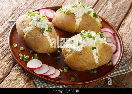 Homemade potatoes stuffed with salted cottage cheese, sour cream and green onions close-up in a plate on a wooden table. Horizontal Stock Photo