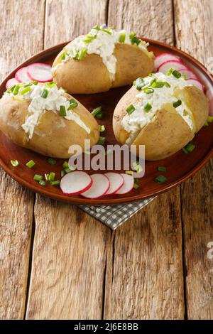Jacket potatoes stuffed with salted curd cheese and green onions close-up in a plate on a wooden table. Vertical Stock Photo