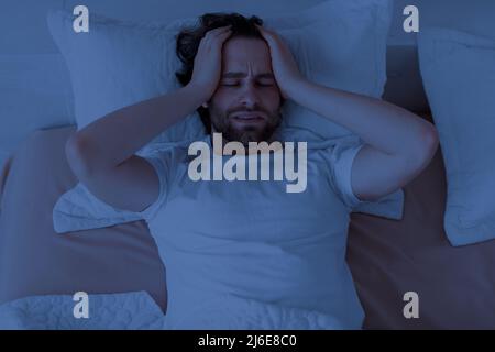 Sleepless guy laying alone in bed, touching his head Stock Photo