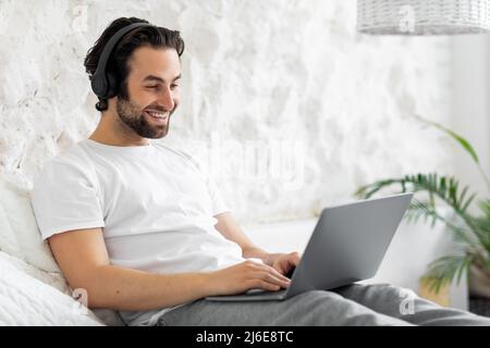 Happy young man sitting on bed, using computer Stock Photo