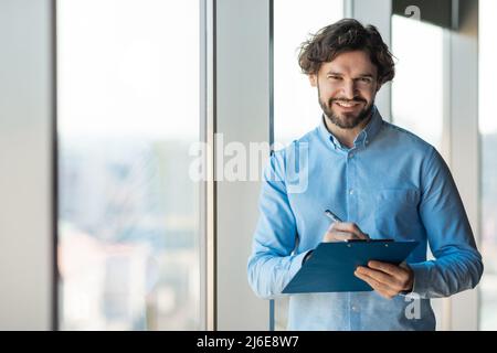 Portrait of confident man looking at camera writing in clipboard Stock Photo