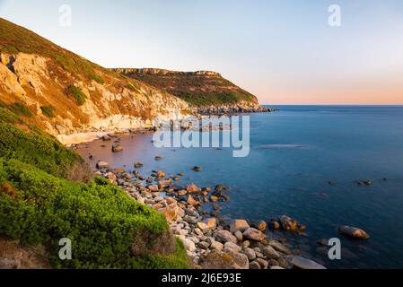 The colourful rocks of the table mountains in the bay of S'Abba Druche and the deep blue Mediterranean Sea in the last light of the sunset, Sardinia Stock Photo