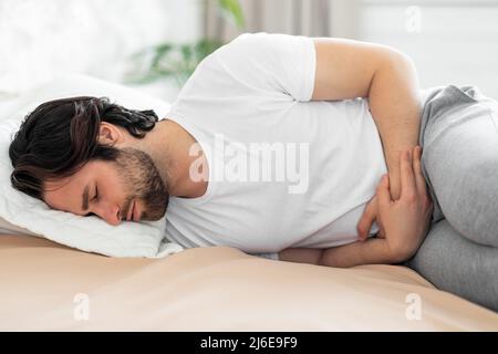 Man lying in bed and suffering from stomach pain Stock Photo