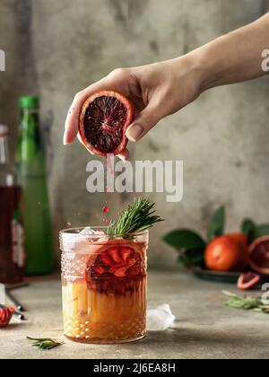 Female hand squeezing juice from orange into a glass with delicious iced cocktail . Frozen drops Stock Photo