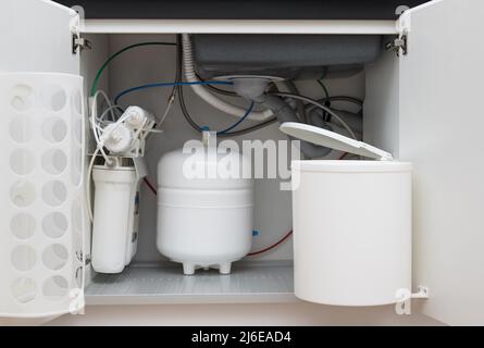 Opened kitchen cabinet with sink, garbage bin, water filtration system Stock Photo