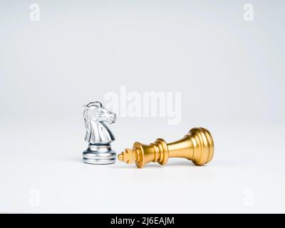 The silver horses, knight chess piece standing near the loser golden king chess piece who fell isolated on white background. Leadership, winner, loser Stock Photo