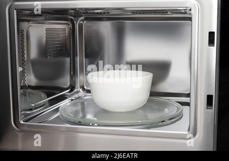 white bowl in modern stainless microwave oven Stock Photo