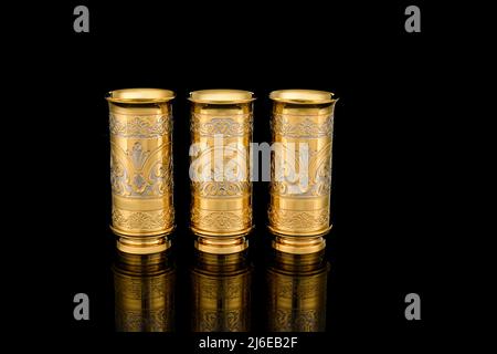 Three Golden Antique Vintage Brass Shot Glass Gilded on black background. metal Wine Cup goblet with Carving Engraving pattern. Stock Photo