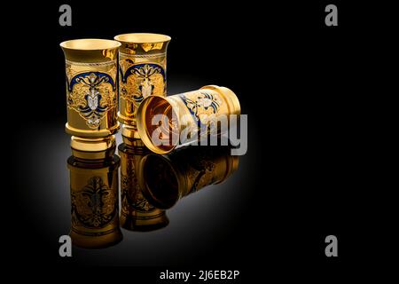 Three Golden Antique Vintage Brass Shot Glass Gilded on black background. metal Wine Cup goblet with Carving Engraving pattern. Stock Photo