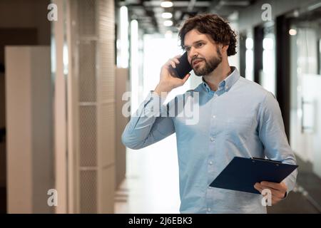 Business man talking on phone at office, holding clipboard Stock Photo