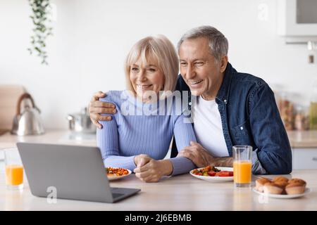 Cheerful senior couple using computer while having breakfast Stock Photo