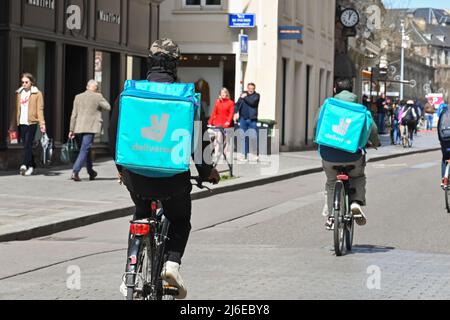 Strasbourg, France - April 2022: Delivery persons with backpacks for Deliveroo riding bicycles on a street in Strasbourg city centre Stock Photo