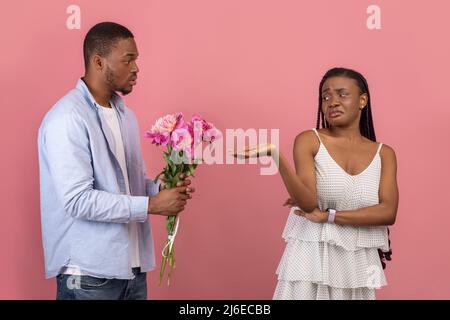 Black man making surprise for bored woman giving flowers Stock Photo