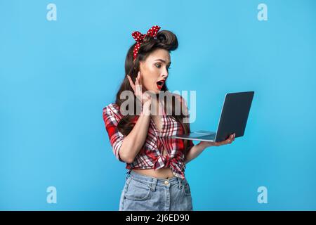 Shocked young pinup lady in retro wear holding laptop pc, shouting in excitement, cannot believe online win or sale Stock Photo