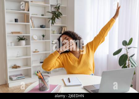 Tired young black female student yawning in front of laptop during online lesson at home Stock Photo