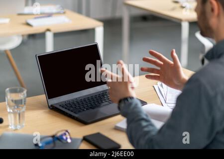 Virtual meeting concept. Back over the shoulder view of mature man sitting at desk, using laptop with black screen Stock Photo