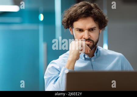 Focused man using laptop sitting at desk in office Stock Photo
