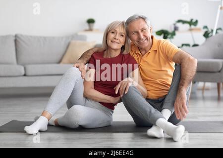 Happy elderly couple sitting on fitness mat at home Stock Photo