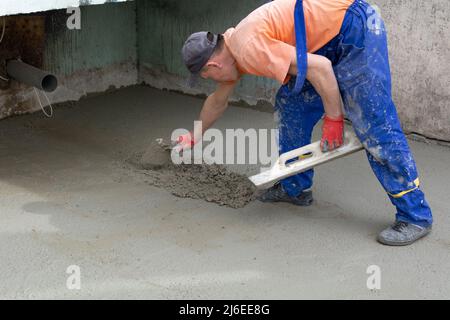 Stormwater construction. An anonymous male construction worker in blue work overalls and an orange construction T-shirt builds a rainwater storm drain Stock Photo