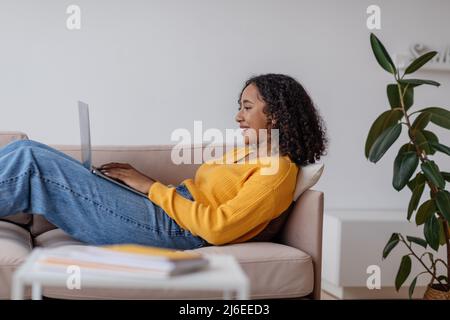 Side view of young African American woman working online via laptop computer in living room Stock Photo