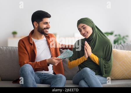 Middle Eastern Husband Giving Money To Wife Sitting At Home Stock Photo