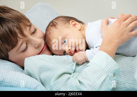 Calm little boy lay in the bed hugging newborn sister Stock Photo