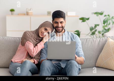 Happy Middle Eastern Spouses Using Laptop Sitting At Home Stock Photo
