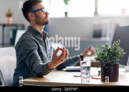 Calm mature male office worker sitting at workdesk with laptop, meditating, relaxing during stressful working day Stock Photo