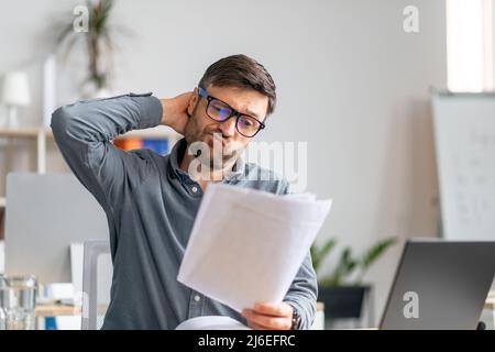 Tired mature male office worker working with documents and having problems, sitting at desk in office Stock Photo