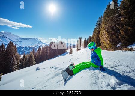 Boy with snowboard sit on the ski track high in mountains Stock Photo