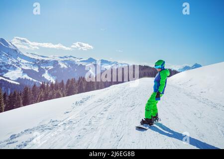 Boy in ski outfit stand on snowboard, sunny view over mountains Stock Photo