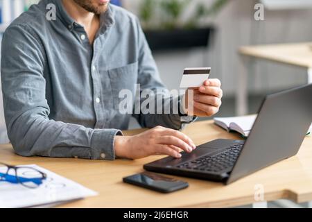 Unrecognizable mature man using laptop and credit card for online payments, sitting at desk in office Stock Photo