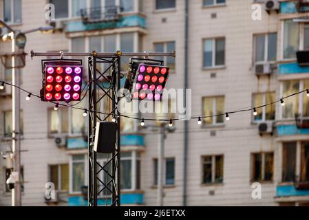 Illumination of a city street with red and pink spotlight lamps on a metal rack at dusk against the backdrop of a residential building in blur. Stock Photo